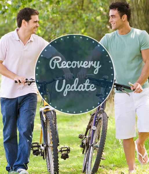 The cover of Recovery Update newsletter: Two male friends carry their bikes in a park.