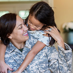 A female soldier is hugged by her daughter from the back.