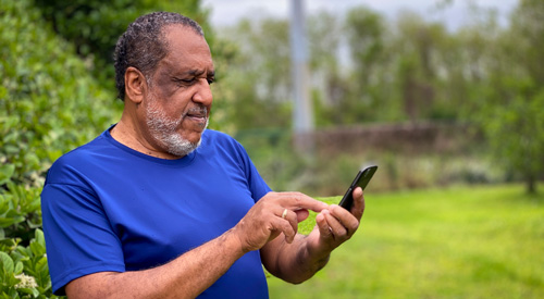 Veteran accessing care on his phone while standing outdoors.