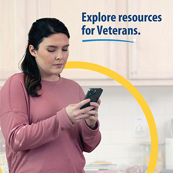 A Veteran  looking at their cellphone screen while in a kitchen. The text reads, “Explore resources for Veterans.” 