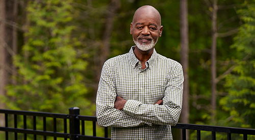 A Veteran standing on a balcony with the woods behind him.